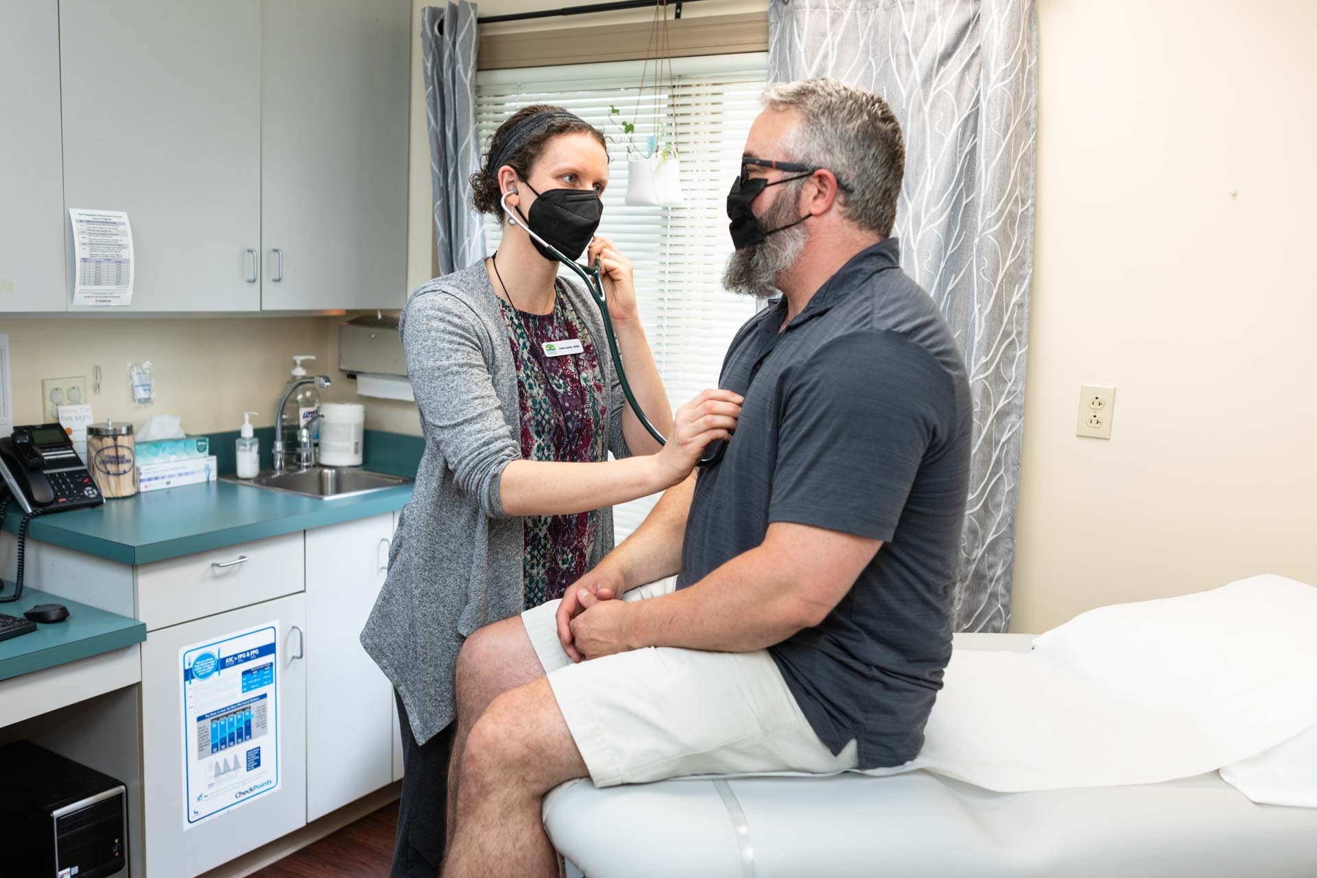 Listening to seated patient's chest with stethoscope